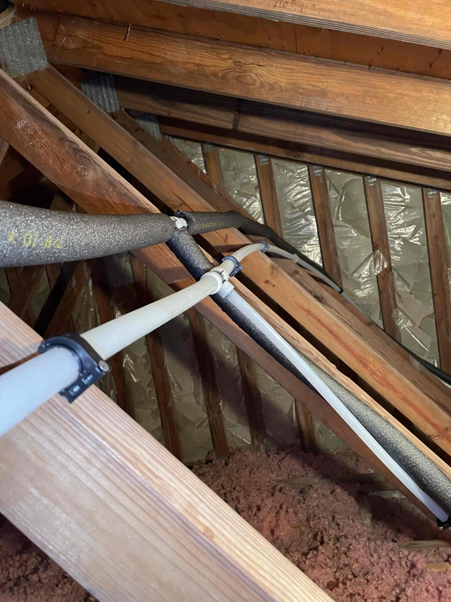 White water lines and black pipe insulation secured along wooden attic framing