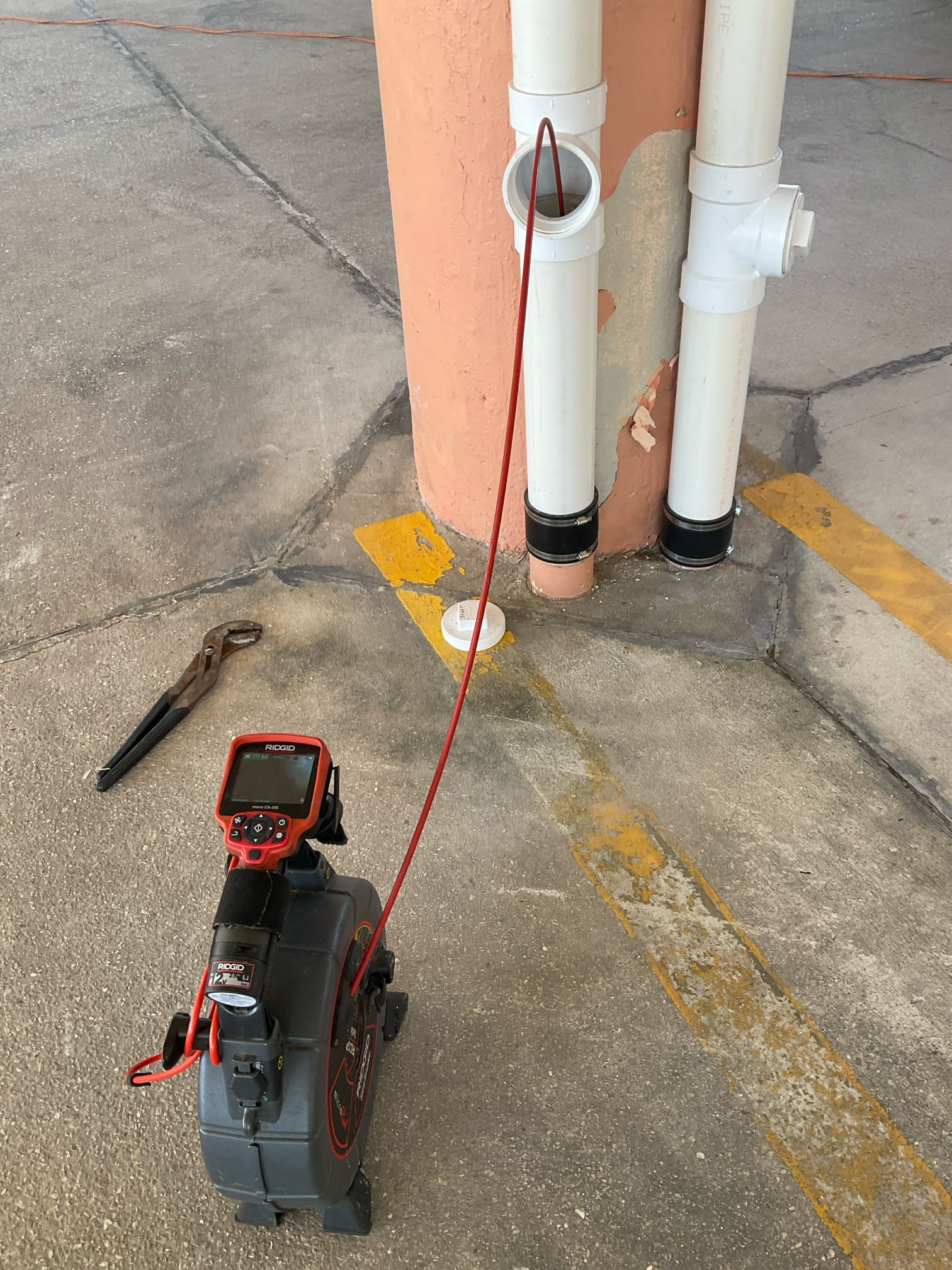 RIDGID sewer camera inspection equipment with red cable at an open vertical pipe cleanout