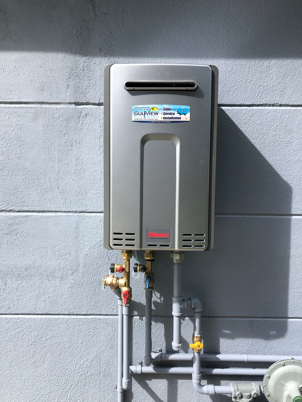 Rinnai tankless water heater with Gulfview service sticker, service valves and connected piping on a gray exterior wall