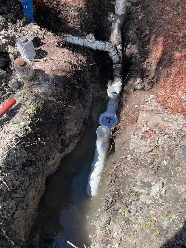 Open backwater valve assembly and white PVC drain piping in an excavated trench.