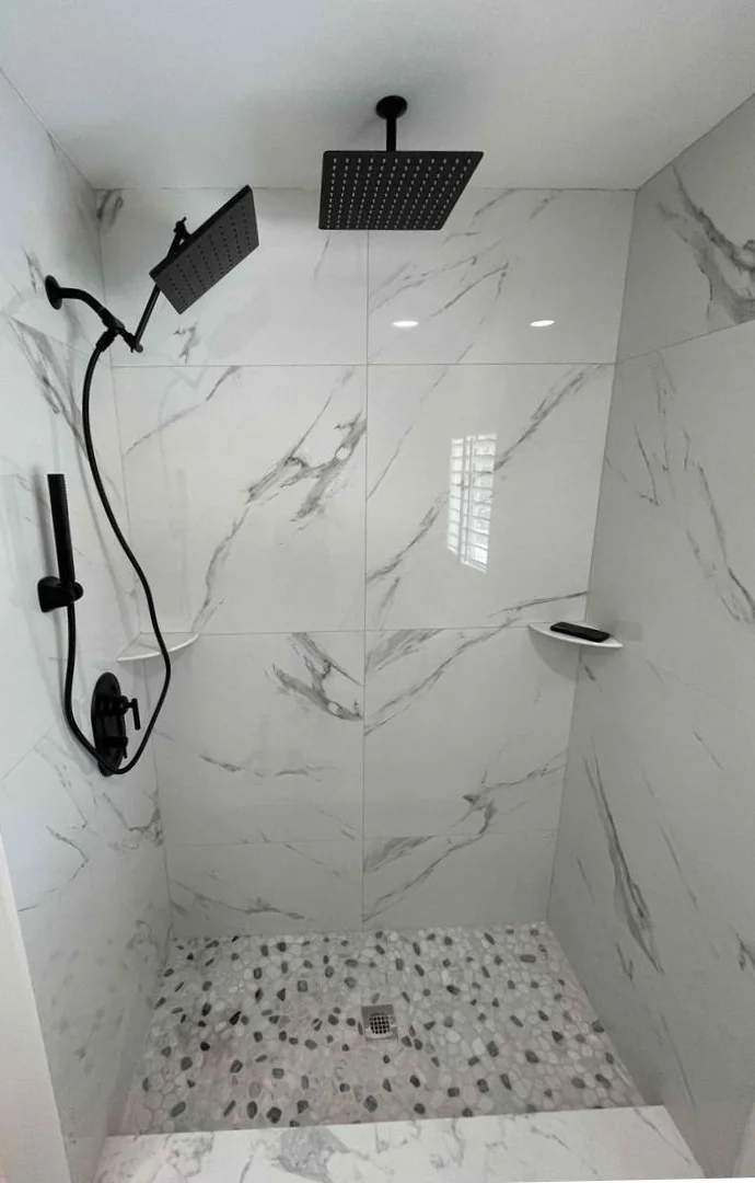 Black shower fixtures with overhead rain head, handheld shower and wall control in a tiled enclosure