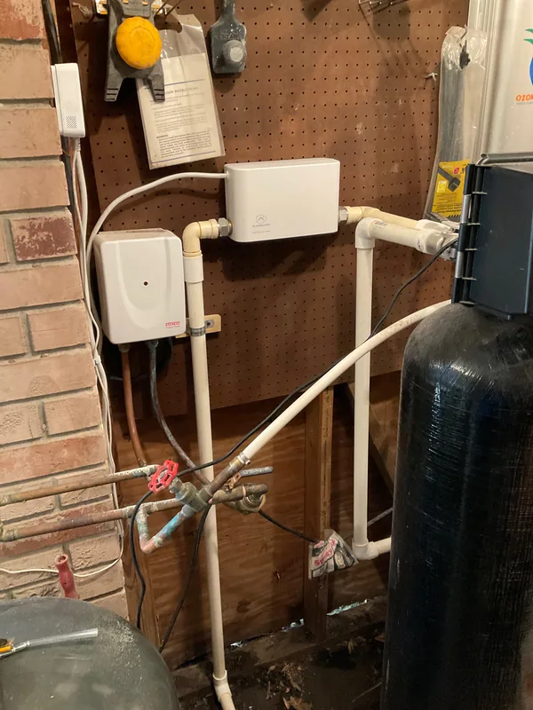 Customer-supplied smart water valve connected to white PVC piping beside existing water-treatment equipment.