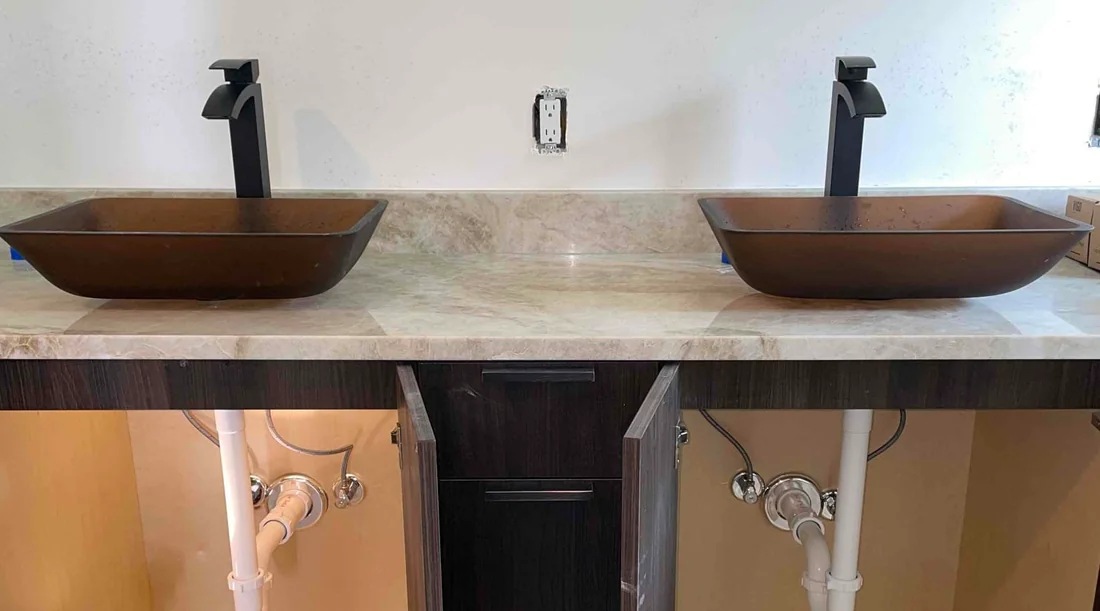 Two brown vessel sinks with black faucets and visible under-sink plumbing during installation