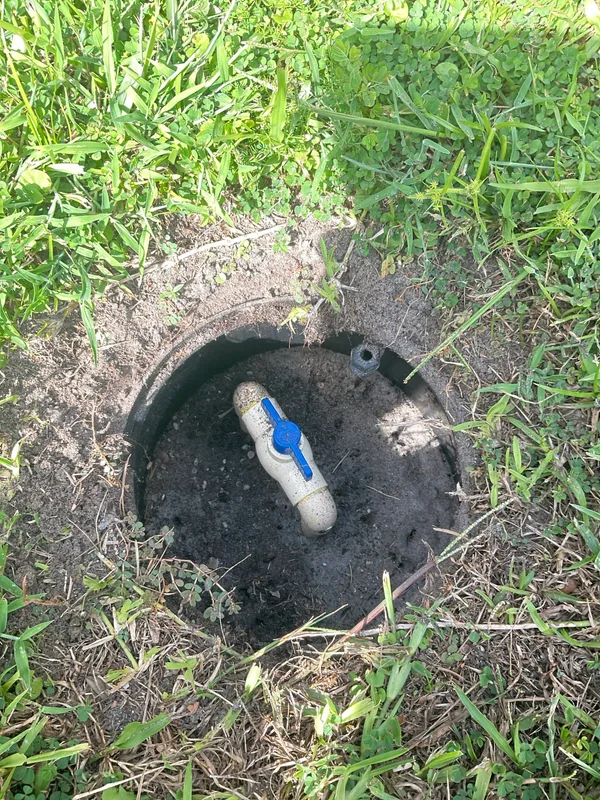 Blue-handled manual water shutoff valve inside a round outdoor access box with the cover removed.