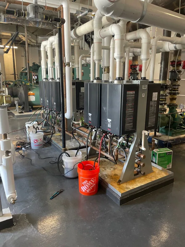 Bank of tankless water heaters with hoses and buckets in a commercial mechanical room