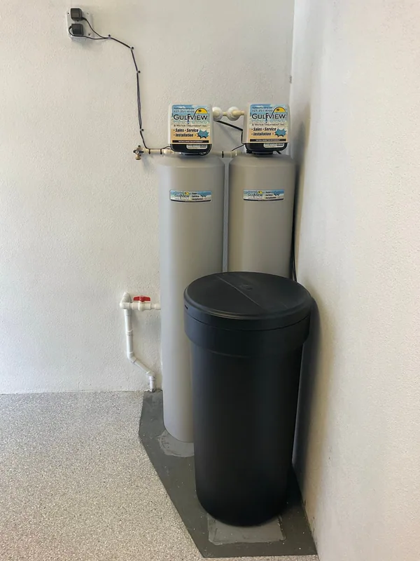 Two Gulfview treatment tanks and a round black brine container in a white utility alcove