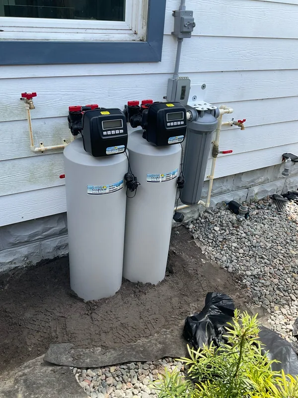 Two gray treatment vessels and a cartridge filter beside white exterior siding