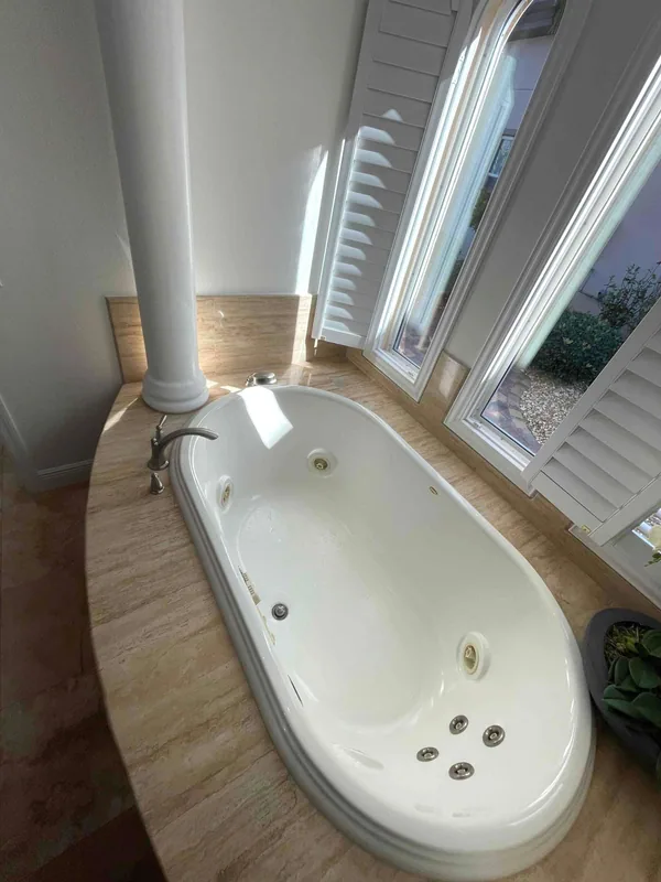 White jetted bathtub with curved deck-mounted faucet beside shuttered bay windows