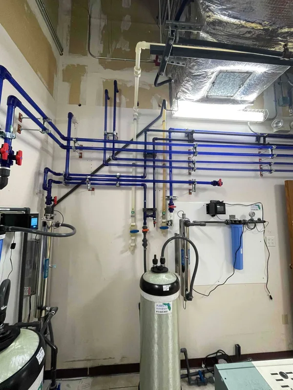 Blue wall-mounted water piping with valves and treatment vessels in a laboratory equipment room