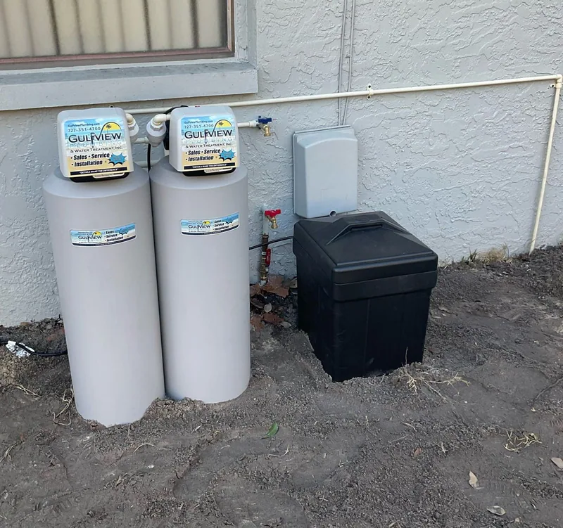 Two gray Gulfview water-treatment tanks and a black brine container below an exterior window