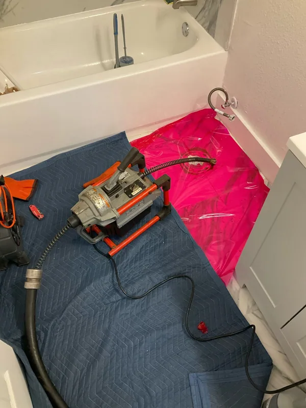 Drain-cleaning machine connected at a toilet drain with protective coverings on the bathroom floor