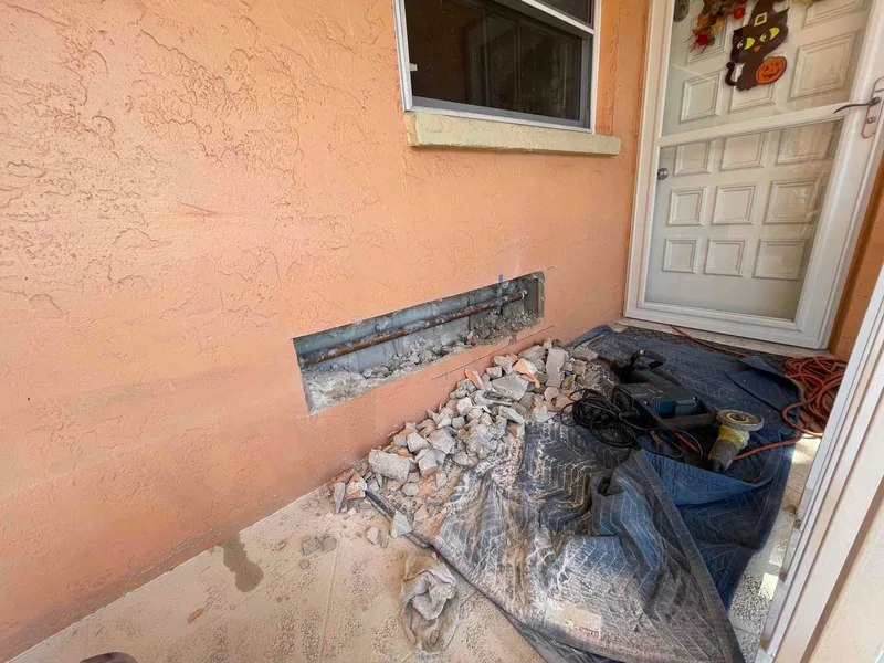 Existing copper waste arm exposed in an opened peach-colored exterior wall