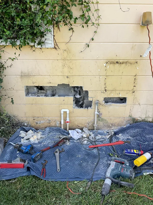 Openings in a yellow exterior block wall exposing drain piping with tools on a protective blanket