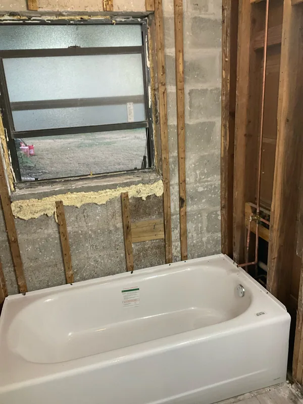 White alcove bathtub with copper piping and exposed wall framing before wall finishes