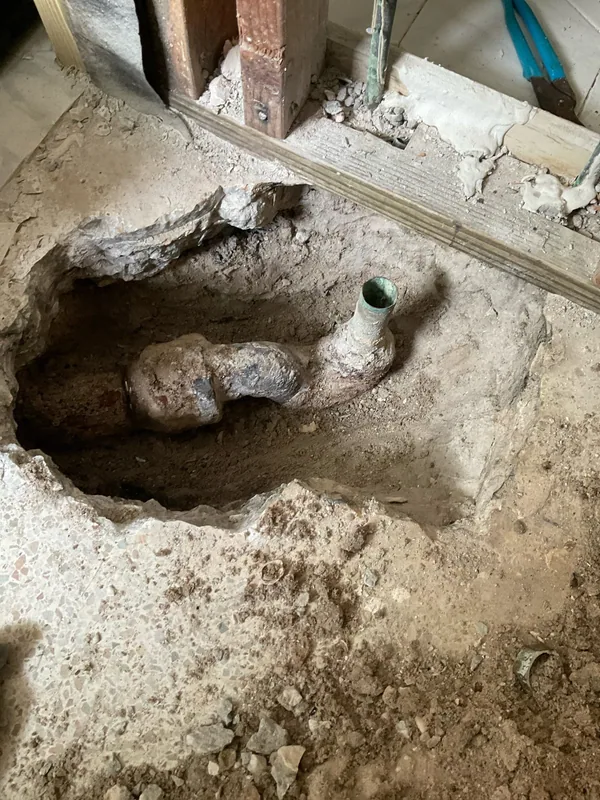 Drain trap and pipe exposed through an opening in a concrete floor beside wall framing