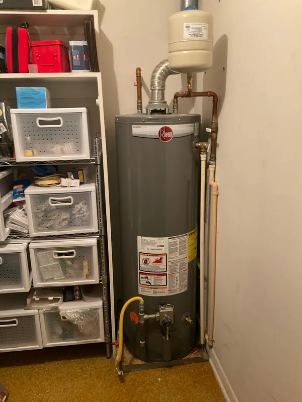 Front view of a Rheem gas tank water heater with overhead expansion tank, vent connector and copper piping