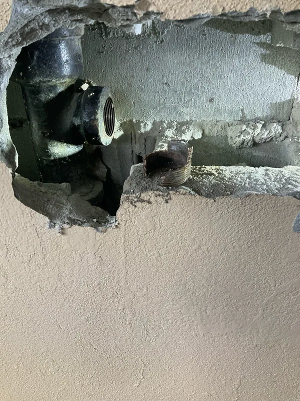 Drain connection exposed through an opening in a cream-colored exterior wall