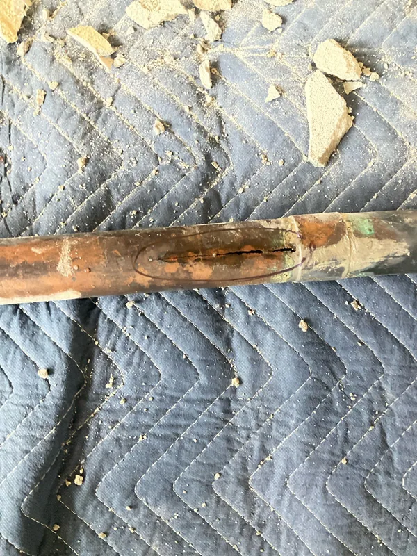 Removed copper waste arm with a visible split marked on the pipe