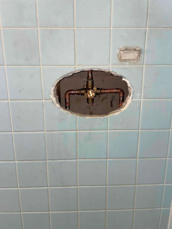 Brass shower valve and copper connections exposed through an opening in blue wall tile