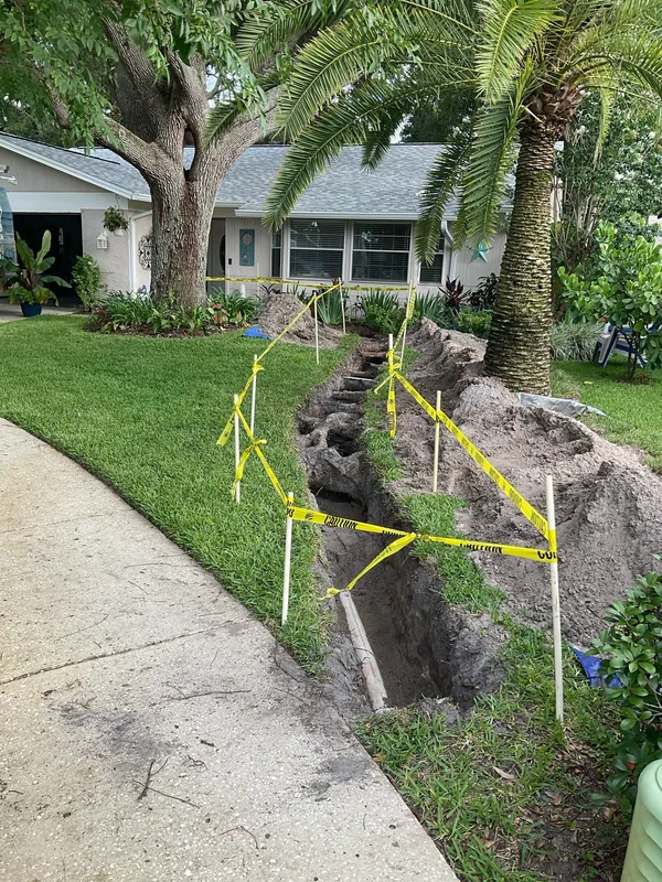 Excavated trench through a front lawn with crossing roots and yellow caution tape