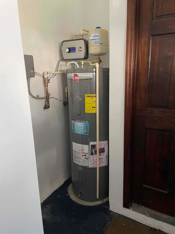 Front view of a Rheem tank water heater with booster and expansion tank in a utility closet