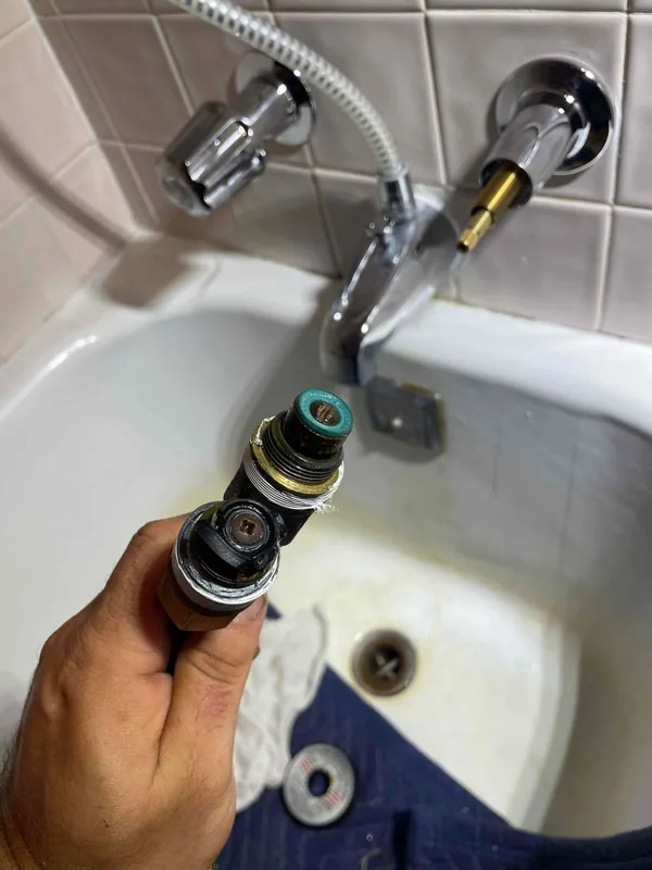 Hand holding removed faucet parts in front of a tub and shower fixture