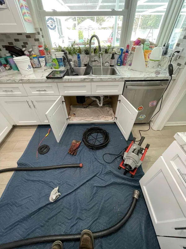 Kitchen drain equipment and open sink cabinet on floor protection, with shoes visible at the edge