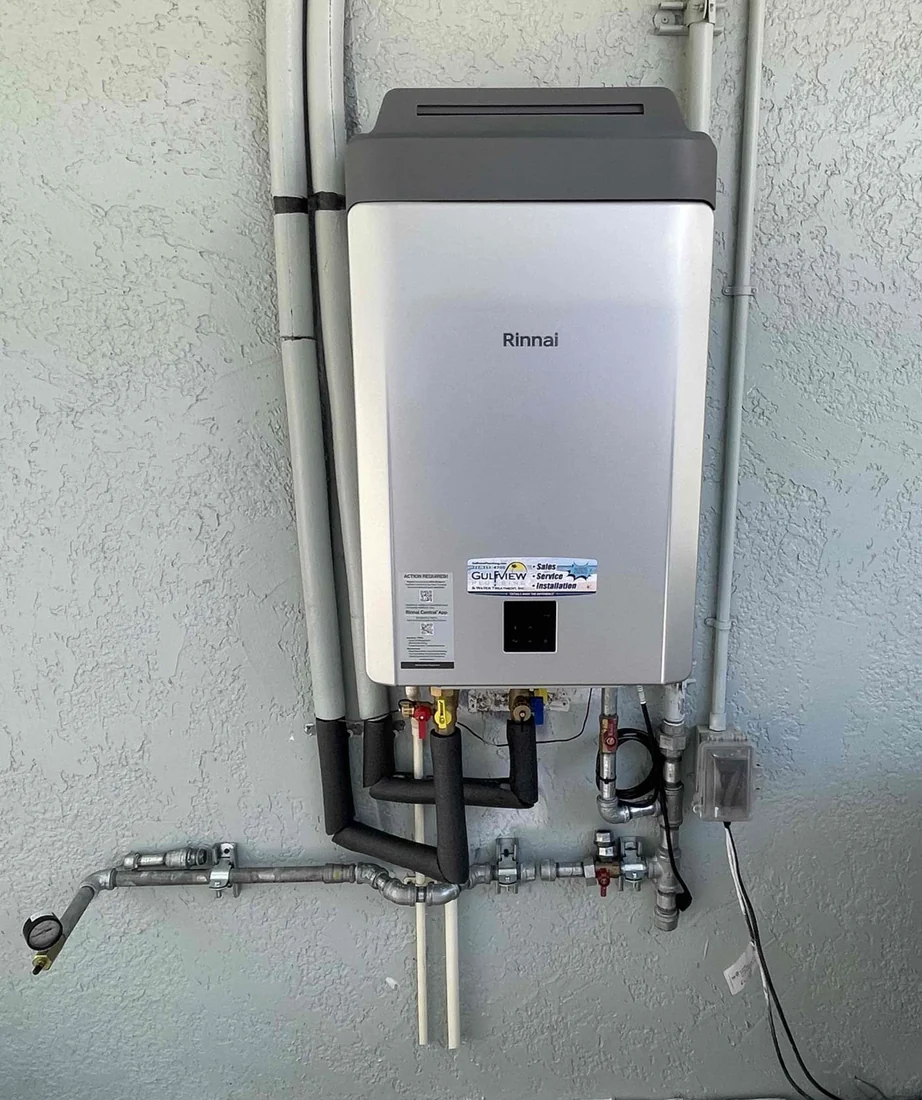 Rinnai tankless water heater on a gray exterior wall with insulated pipes and service connections.