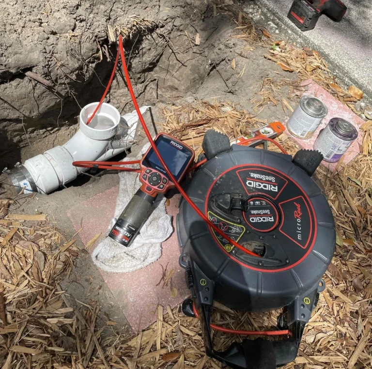 RIDGID sewer inspection camera and red cable positioned beside exposed PVC cleanout piping.