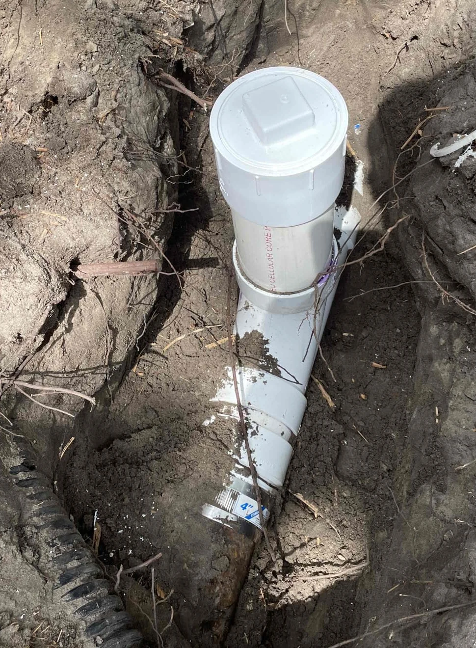 New capped PVC sewer cleanout and pipe connections exposed in a trench before backfill.