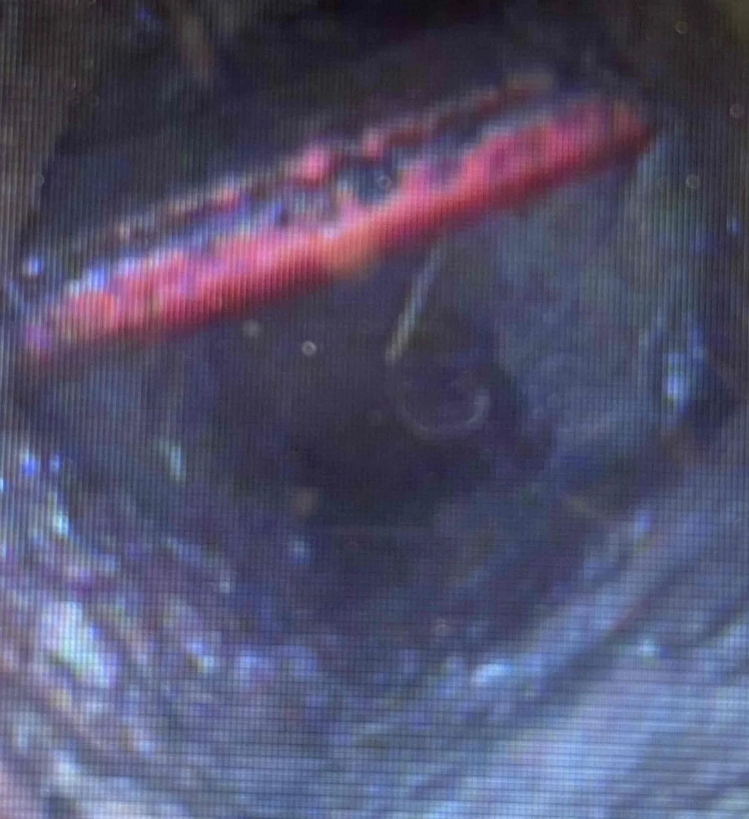 Cropped sewer-camera monitor view showing a red utility line crossing the interior of a drain pipe.