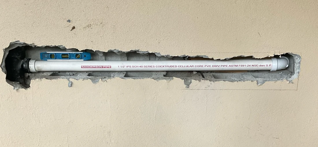 White PVC waste arm exposed in a horizontal wall opening during replacement.