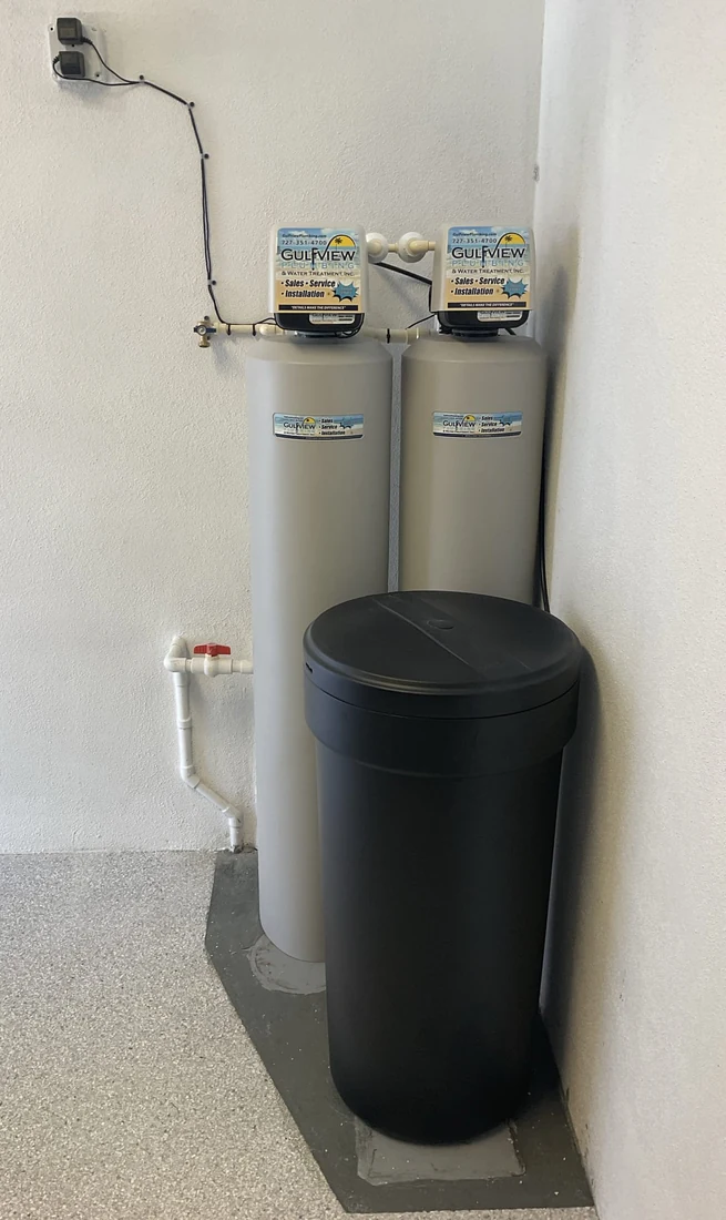 Two water-treatment tanks and a black brine tank installed in a corner.