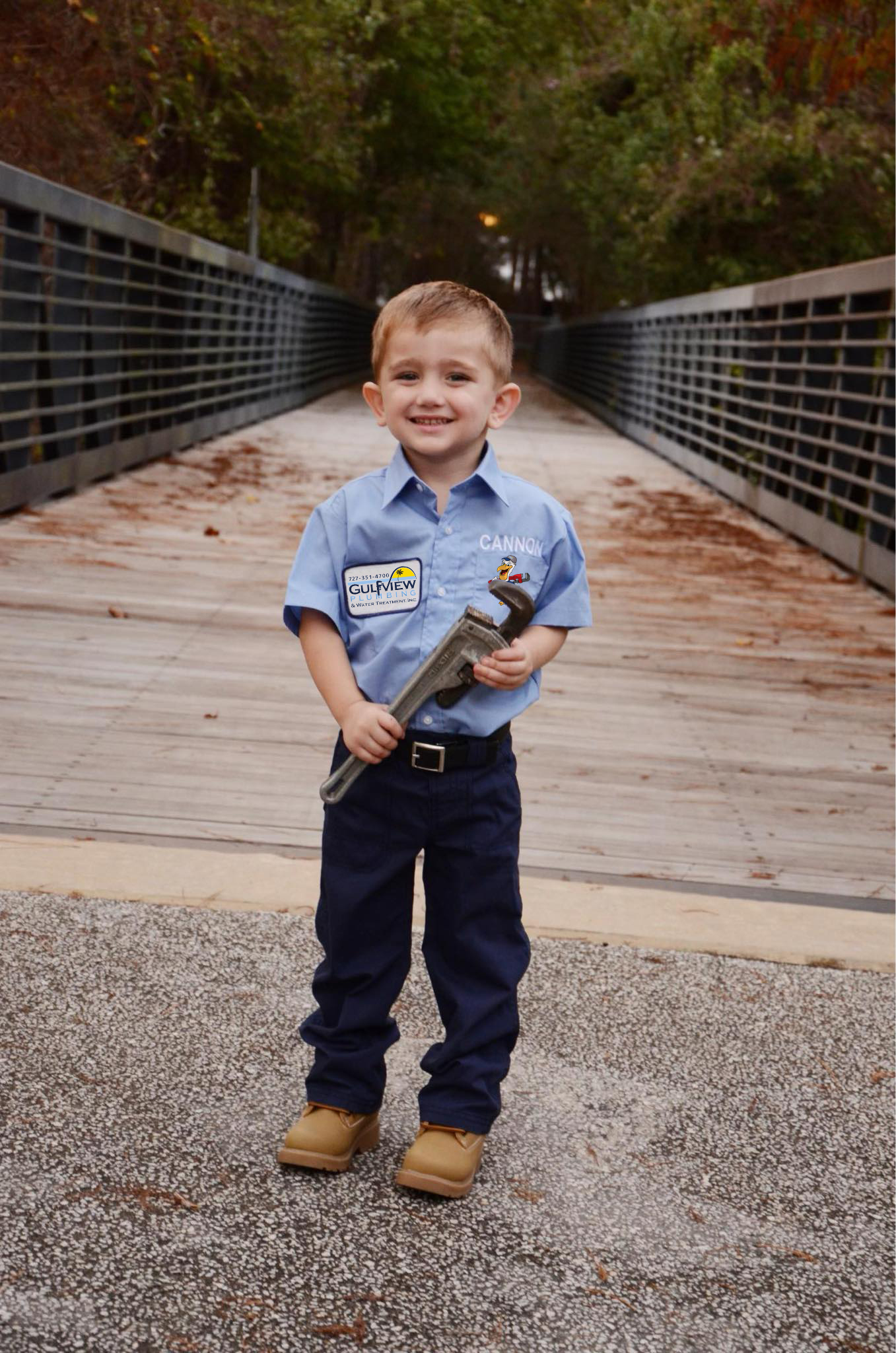Young boy in a blue Gulfview shirt holding a pipe wrench on a wooden bridge