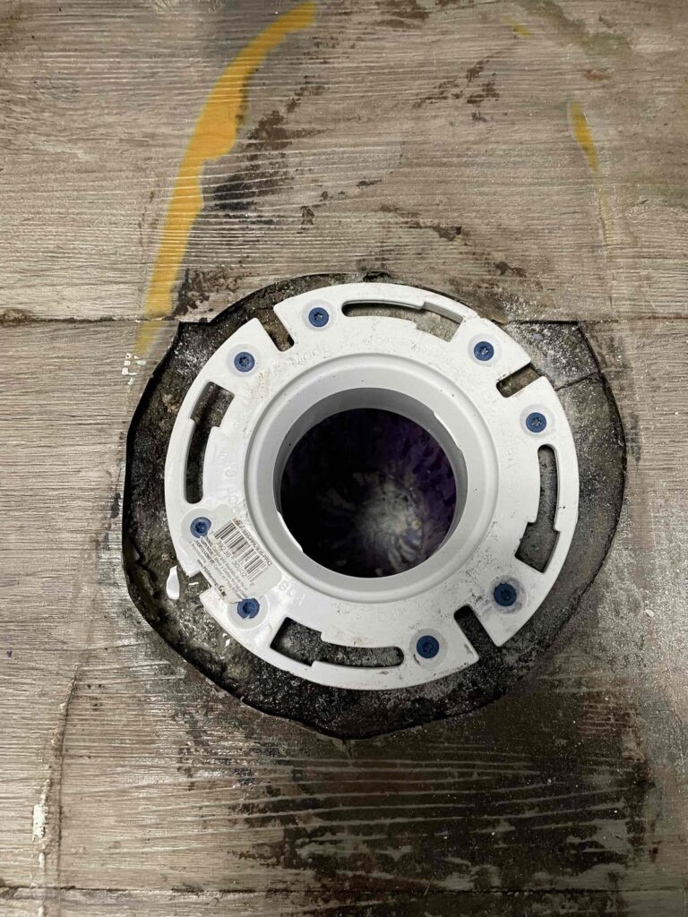 Replacement white toilet flange secured at the drain opening