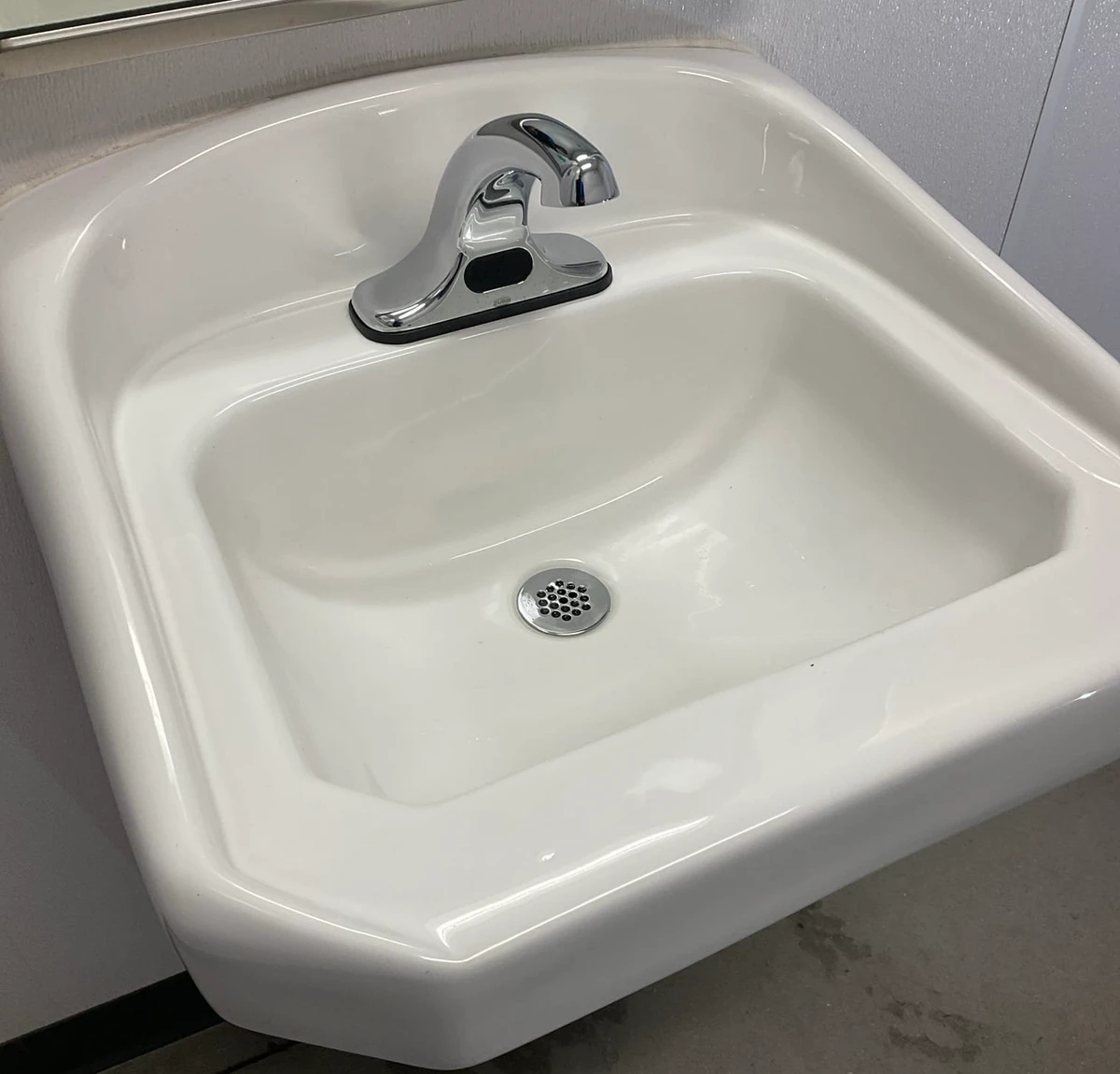 Chrome sensor-operated faucet on a white commercial restroom sink