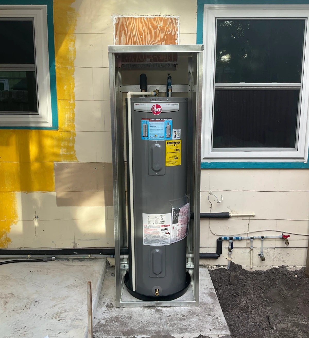 Rheem tank water heater installed inside an open outdoor metal enclosure