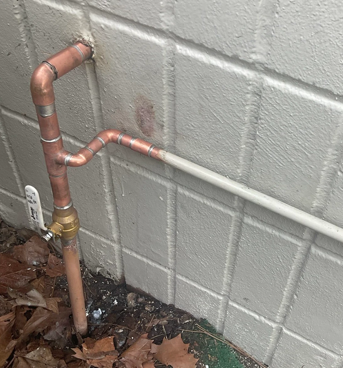 Replacement brass shutoff valve and reworked copper water piping beside an exterior block wall