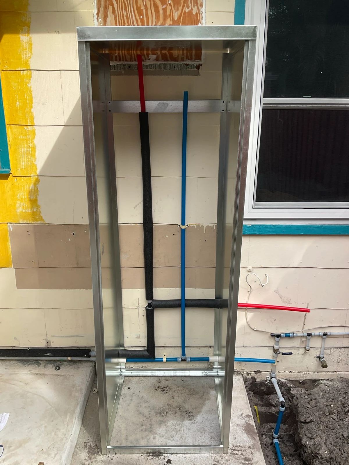 Open outdoor water heater enclosure with piping and insulation before the tank is placed
