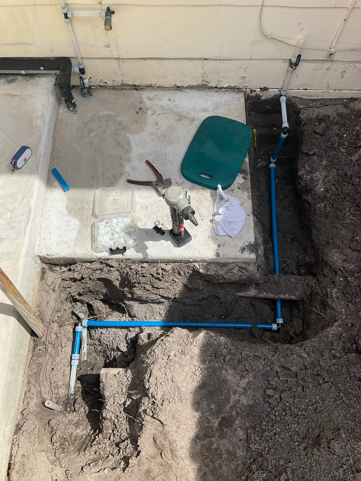 Water piping exposed in a trench beside the concrete pad for an outdoor water heater project
